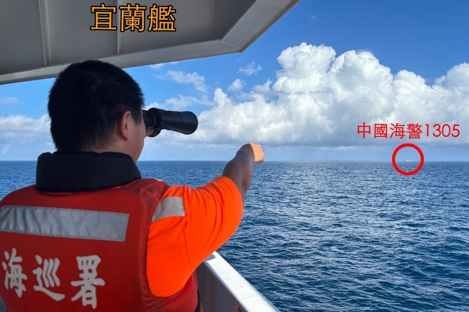 A Taiwan Coast Guard member uses binoculars on a patrol ship off Pengjia Islet (Keelung) while pointing at a Chinese Coast Guard ship sailing in the distance.