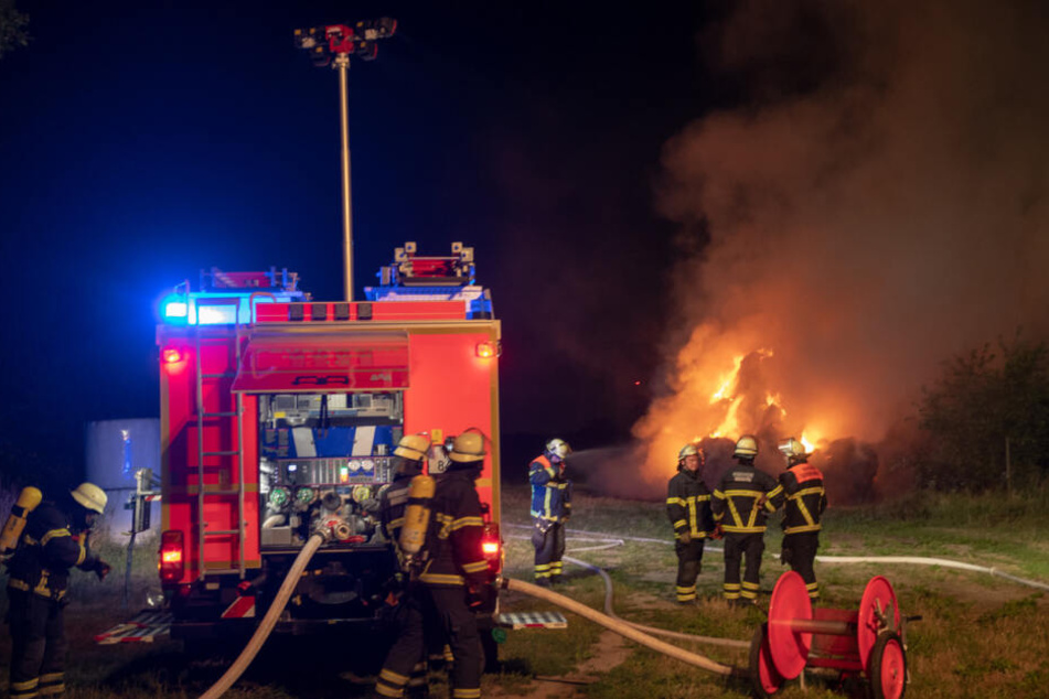 Einsatzkräfte stehen vor den brennenden Heuballen.