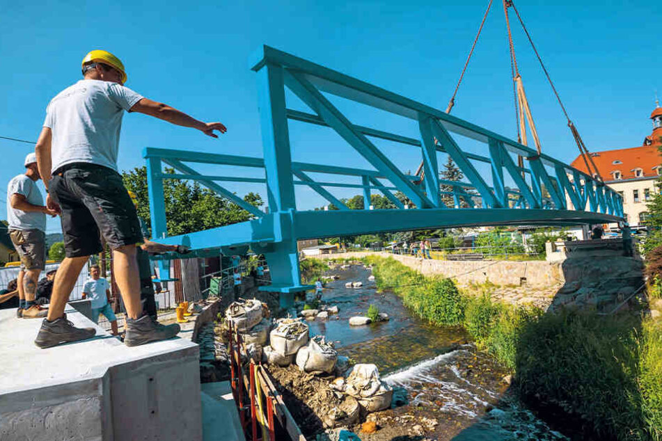 Hier muss alles ganz genau passen: Mit einem Kran wird die neue Fußgängerbrücke über die Zwönitz auf den Unterbau gesetzt.