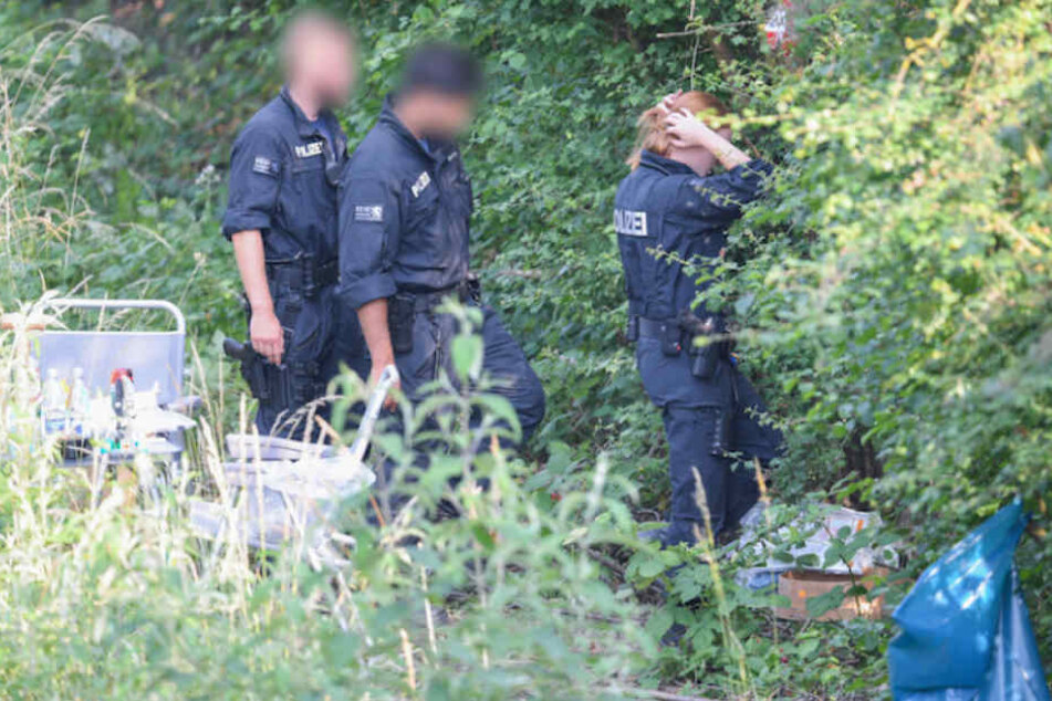 Polizisten suchen den Fundort der Leiche im Gebüsch ab. (Symbolbild)