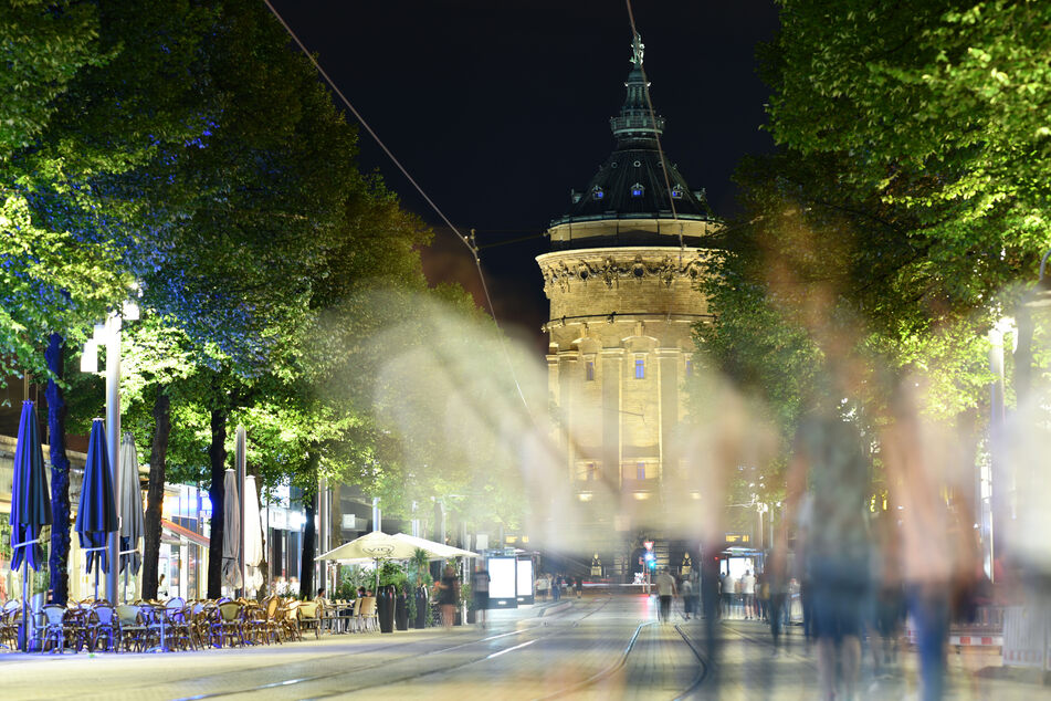Menschen gehen am späten Abend in der Fußgängerzone Mannheims vor dem Wasserturm.