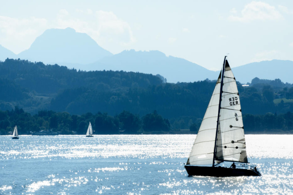 Das Wasser auf dem Chiemsee glitzert rund um ein Segelboot.