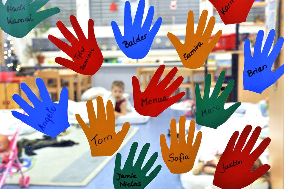 Ausgeschnittene Hände mit Kindernamen hängen mit den jeweiligen Namen an der Eingangstür einer Kindergruppe. (Symbolbild)