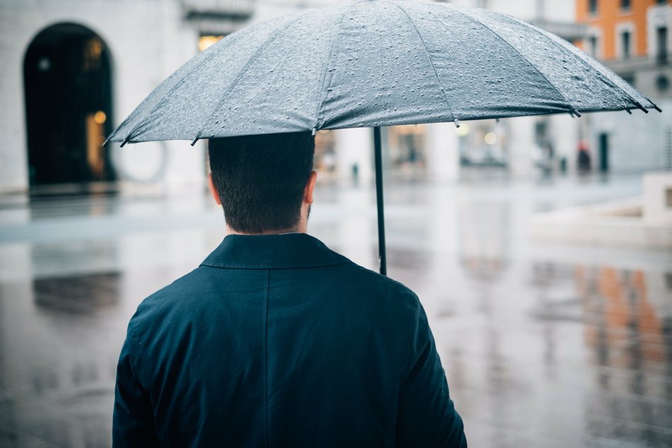 Ein Mann schützt sich mit einem Schirm vor herbstlichem Nieselregen. (Symbolbild)