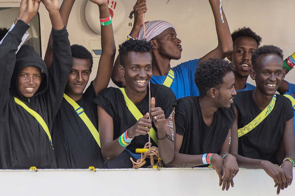 Migranten und Besatzungsmitglieder des Rettungsschiffes Aquarius winken beim Einlaufen in den Hafen von Senglea. (Symbolbild/Archivbild)