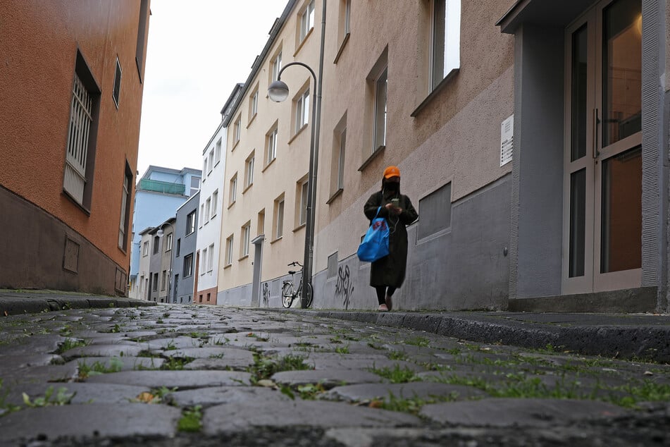 Eine Frau mit einem Tuch vor Mund und Nase geht durch eine Gasse. Nach den vorliegenden Zahlen gelten mittlerweile fast alle Regionen in NRW als Corona-Risikogebiete.