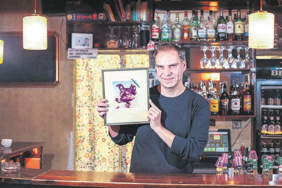 „Laika“-Chef Kristian Münder (48) zeigt das Kneipenfoto Laikas mit
Trauerflor: Am Freitag gibt‘s einen speziellen Laika-Cocktail.