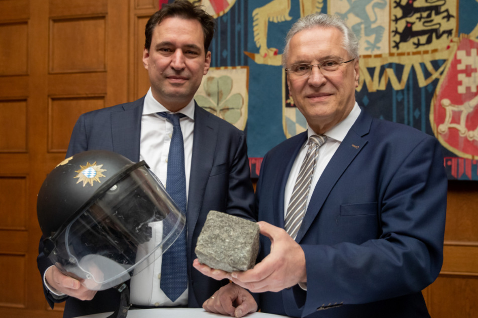 Georg Eisenreich (l), Justizminister von Bayern, und Joachim Herrmann (beide CSU), Innenminister von Bayern, stehen mit einem Polizeihelm, der beim G20-Gipfel 2017 in Hamburg durch einen Pflasterstein beschädigt wurde, in den Händen nebeneinander.