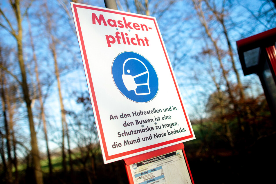 Ein Schild mit der Aufschrift "Maskenpflicht" hängt an einer Bushaltestelle.
