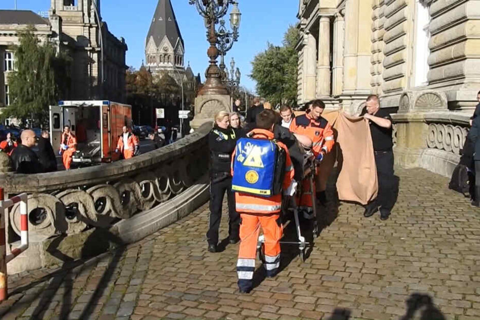 Ein verletzter Mann wird von Sanitätern und Polizisten vor dem Strafjustizgebäude zu einem Rettungswagen gebracht.