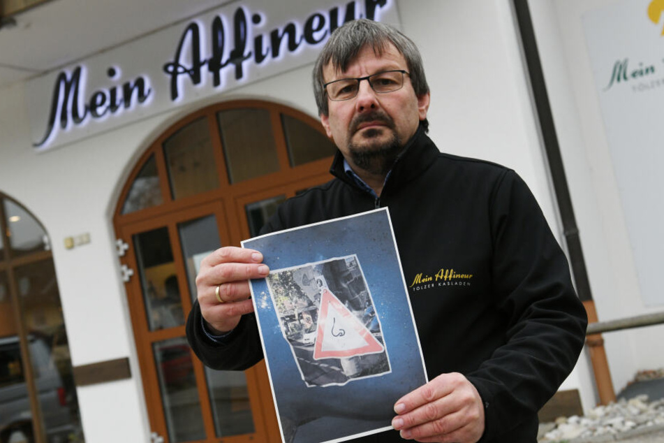 Der Geschäftsführer des Tölzer Kasladen, Wolfgang Hofmann steht mit einem Foto der Protestschilder vor seinem Laden. Der Käse aus dem Kasladen beschäftig seit Längerem die Gerichte.