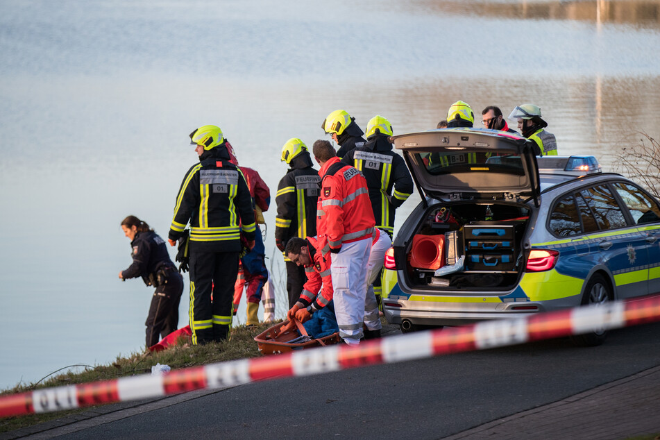 Einsatzkräfte der Polizei und Feuerwehr stehen am Ufer eines Sees. (Symbolbild)