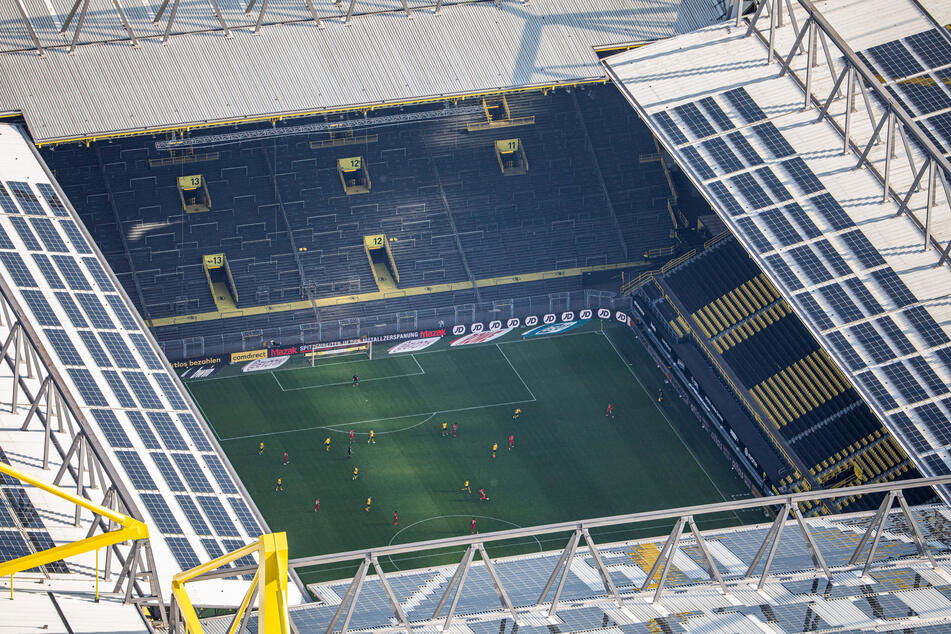 Fußballer zweier Mannschaften (Dortmund in gelb) bestreiten eine Partie vor leeren Zuschauerrängen.