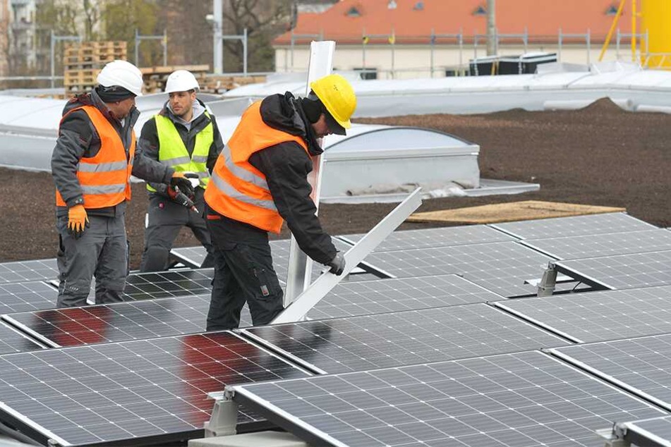 Arbeiter montieren auf dem Dach der neuen Halle Photovoltaikmodule.