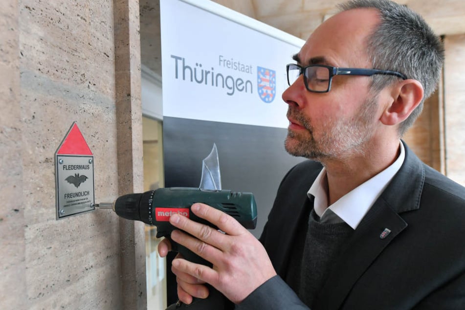 Olaf Möller, Staatssekretär im Thüringer Ministerium für Umwelt, Energie und Naturschutz, schraubt die Auszeichnungs-Plakette an eine Mauer des Umweltministeriums.