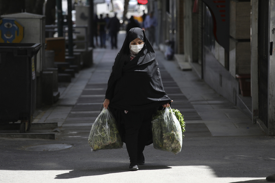 Eine Frau mit Mundschutz, als Maßnahme gegen die Ausbreitung des Coronavirus, trägt Tüten mit Einkäufen.