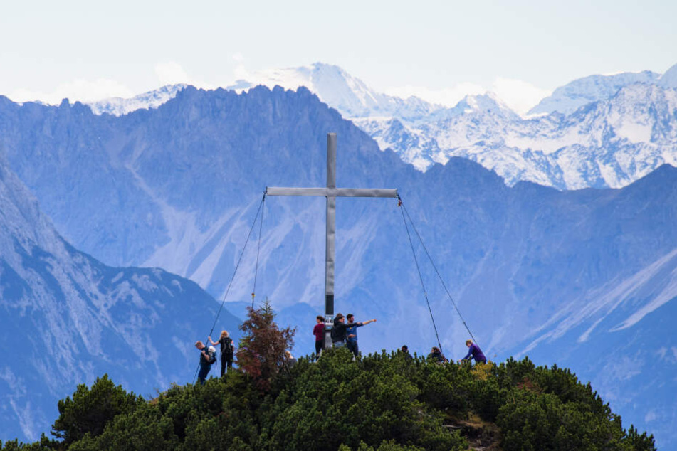 Wanderer stehten neben dem Gipfelkreuz vom Martinskopf bei Walchensee.