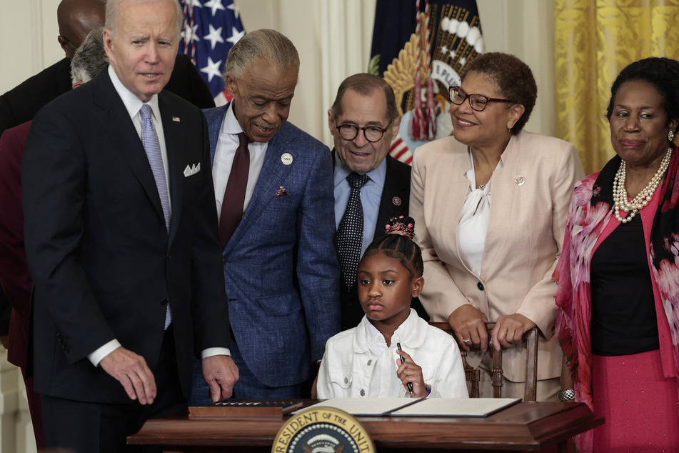 Gianna Floyd (bottom c.), the daughter of George Floyd, holds a pen used by U.S. President Joe Biden (l.) to sign an executive order enacting further police reform in the East Room of the White House on May 25, 2022.
