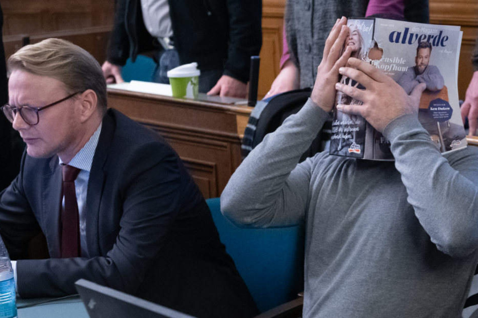 Einer der Angeklagten verdeckt sein Gesicht mit einer Zeitschrift.