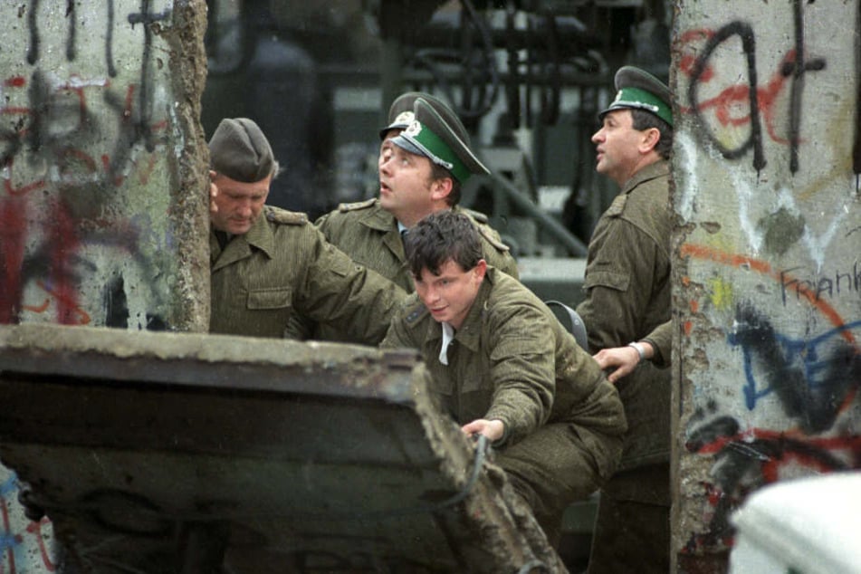 DDR-Grenzsoldaten schließen ein Loch, das Jugendliche in die Berliner Mauer gestemmt haben.
