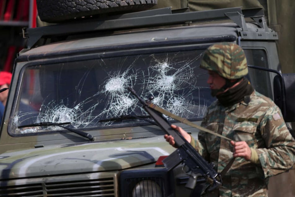 Ein griechischer Soldat patrouilliert am Grenzübergang in Kastanies neben einem Militärfahrzeug mit gebrochener Windschutzscheibe.
