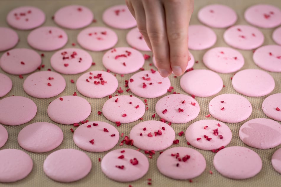 Macarons sehen einfach aus, aber die Herstellung verlangt Geduld, Fingerspitzen-Gefühl und Timing. Flamingo-farbene Makronen werden mit Streuseln verziert.