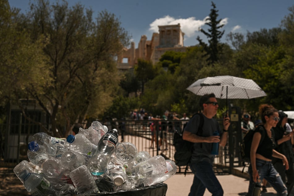Urlauber gehen in der Nähe des Akropolis-Hügels an einem mit Plastikflaschen überfüllten Mülleimer vorbei.