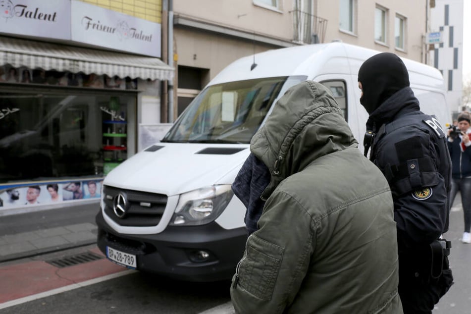 Ein Bundespolizist führt einen festgenommenen Mann zu einem Polizeifahrzeug.