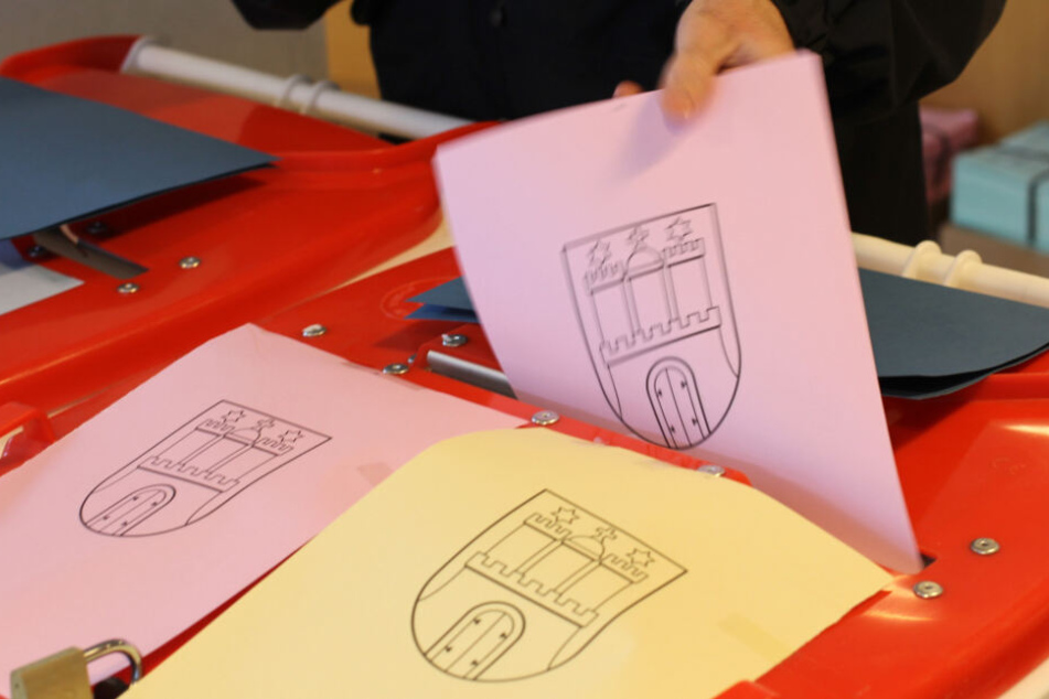 Eine Person schmeißt seine Wahlzettel in die Urne.