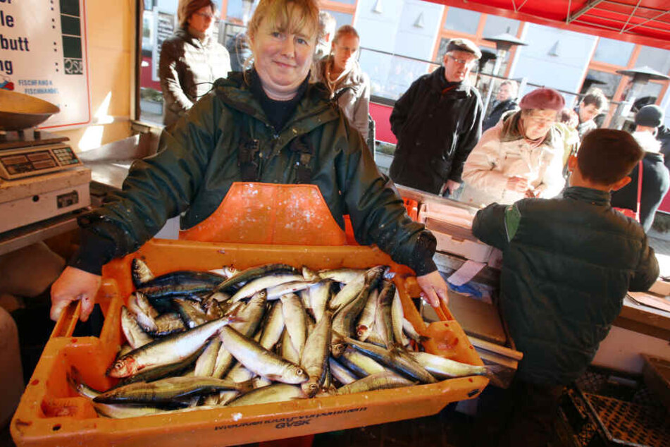 Eine Fischverkäuferin im Ostseebad Warnemünde stellt einen Kasten mit frisch gefangenen Heringen zum Verkauf bereit. (Archivbild)