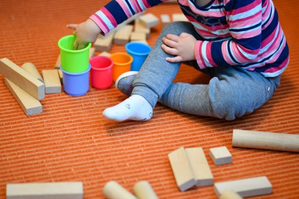 Ein Mädchen spielt in einer Kita mit bunten Bechern und Bauklötzen.