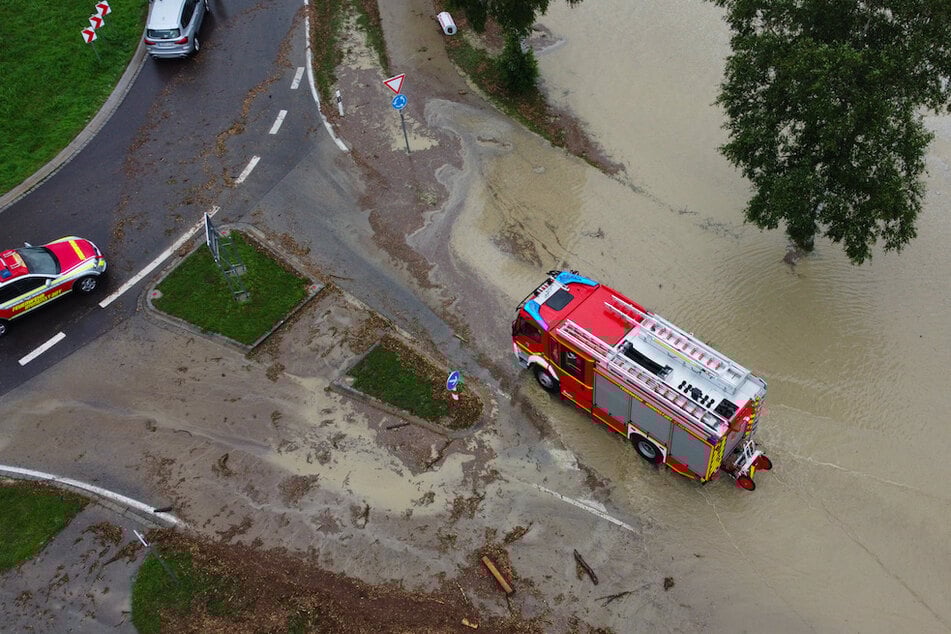 Ein Feuerwehrfahrzeug fährt durch das hoch stehende Wasser an einem Kreisverkehr vor Rettenberg.