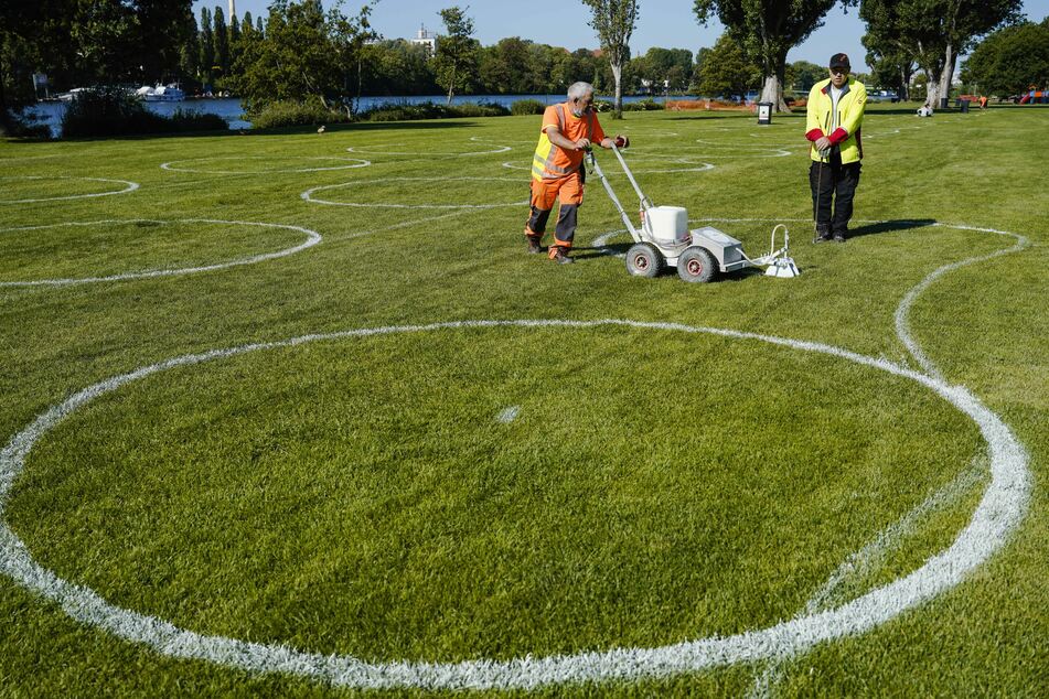 Städtische Mitarbeiter bringen mit Hilfe einer Maschine Rasenmarkierfarbe auf der Neckarwiese auf.