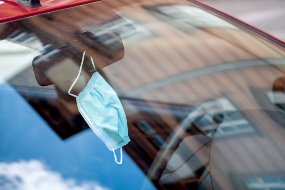 Ein Mund-Nasenschutz hängt an einem Autospiegel.