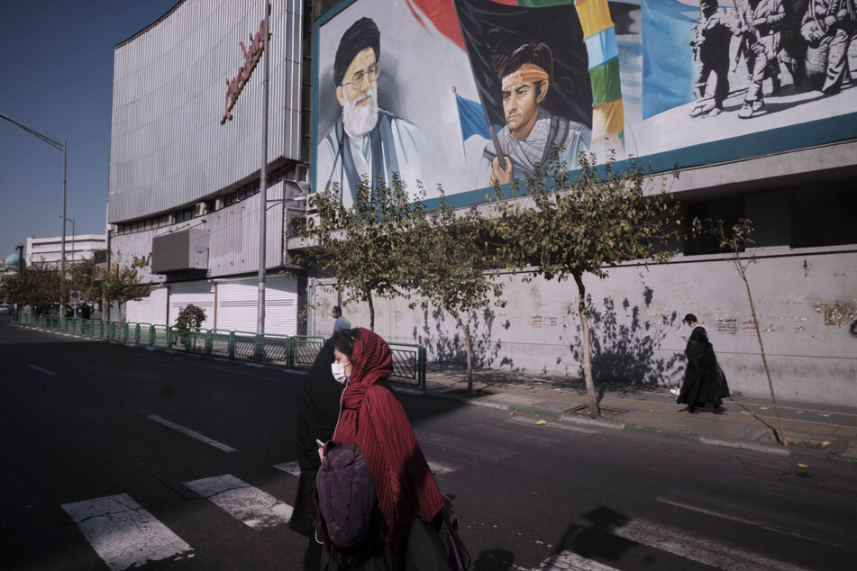 An Iranian woman wearing a protective face mask walks under a portrait of Iran's Supreme Leader Ayatollah Ali Khamenei near the University of Tehran.