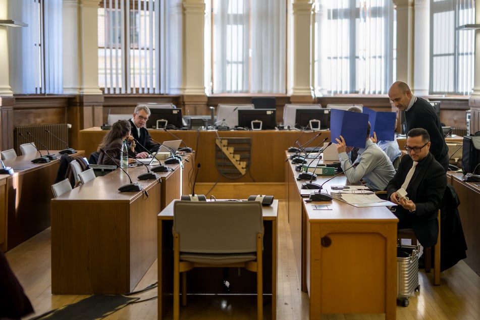 Die Angeklagten, die ihre Gesichter hinter Pappheftern verbargen, mit ihren Anwälten.