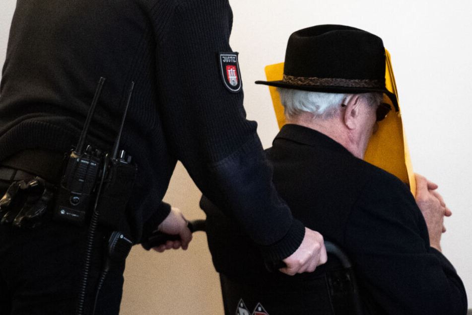 Der Angeklagte wird in einem Rollstuhl aus dem Gerichtssaal gebracht.