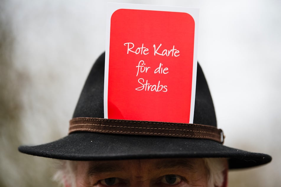 Ein Teilnehmer einer Kundgebung trägt eine Karte mit der Aufschrift "Rote Karte für die Strabs!" hinter seinem Hutband. (Archivbild)