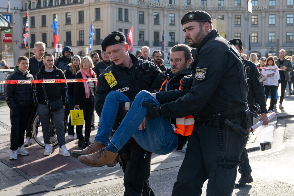 Polizisten tragen einen Klimaaktivisten weg, der sich zuvor am Karlsplatz in der Münchner Innenstadt auf die Straße geklebt hatte.