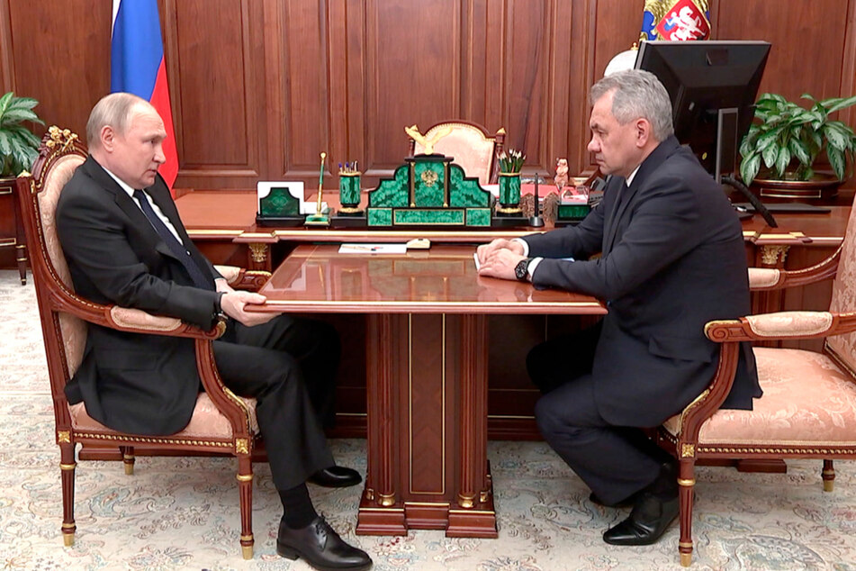 Wladimir Putin (69, l.) und Russlands Verteidigungsminister Sergej Schoigu (67) bei einem Gespräch im Kreml. Putin macht ein zum Teil schmerzverzerrtes Gesicht und hält sich krampfhaft am Tisch fest.