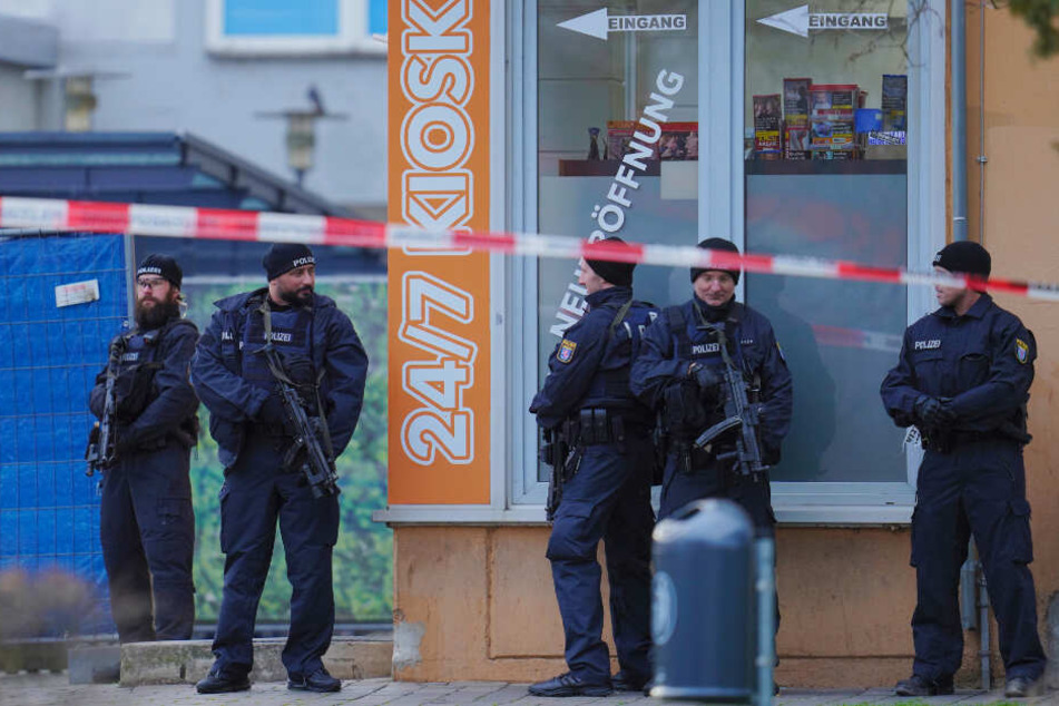 Einsatzkräfte stehen nahe eines Tatorts vor einem Kiosk.