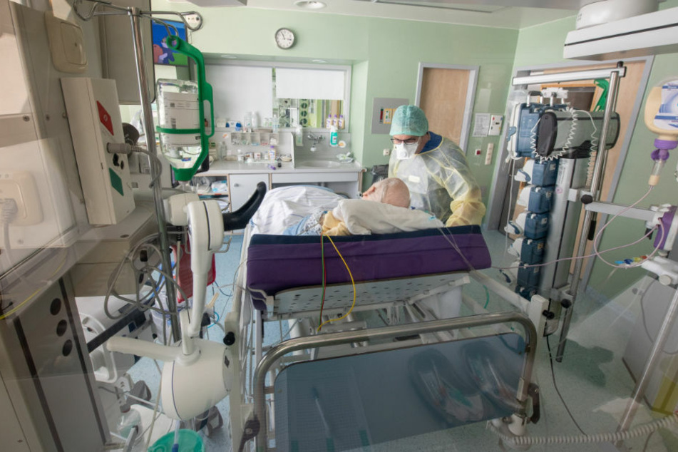 Ein Arzt untersucht in Schutzkleidung in einem isoliertem Intensivbett-Zimmer einen positiv getesteten Corona-Patienten. In Brandenburg sind zwei weitere Menschen an dem Virus gestorben (Symbolfoto)