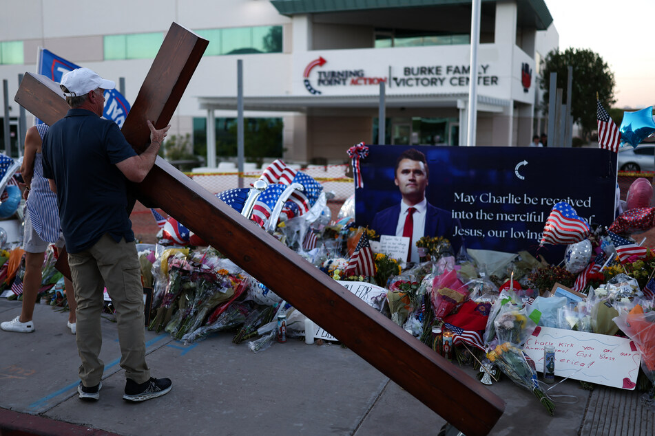A man carries a large cross near a makeshift memorial for Turning Point USA Founder Charlie Kirk outside of the Turning Point USA headquarters in Phoenix, Arizona, on Friday.