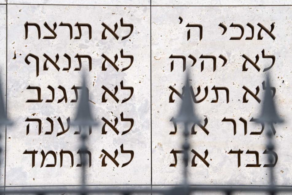 Ein Zaun steht in Stuttgart vor der Synagoge der Israelitischen Religionsgemeinschaft, auf deren Wand im Hintergrund die ersten Worte der zehn Gebote in hebräisch geschrieben sind.