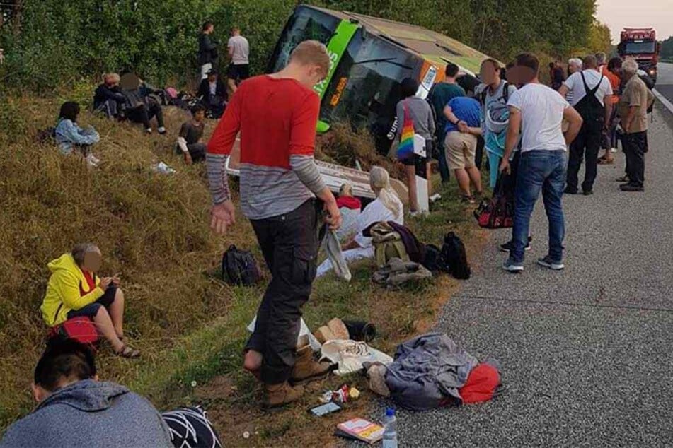 Reisende sitzen um den verunglückten "FlixBus" auf dem Boden.