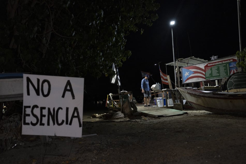 A "No a Esencia" sign stands in the foreground as a fisherman cleans his catch in the Boqueron beach neighborhood in Cabo Rojo, Puerto Rico, on July 15, 2025.