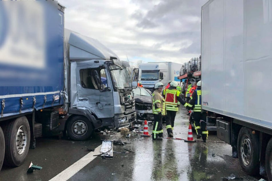 Rettungskräfte stehen auf der A6 zwischen beschädigten Lastwagen.