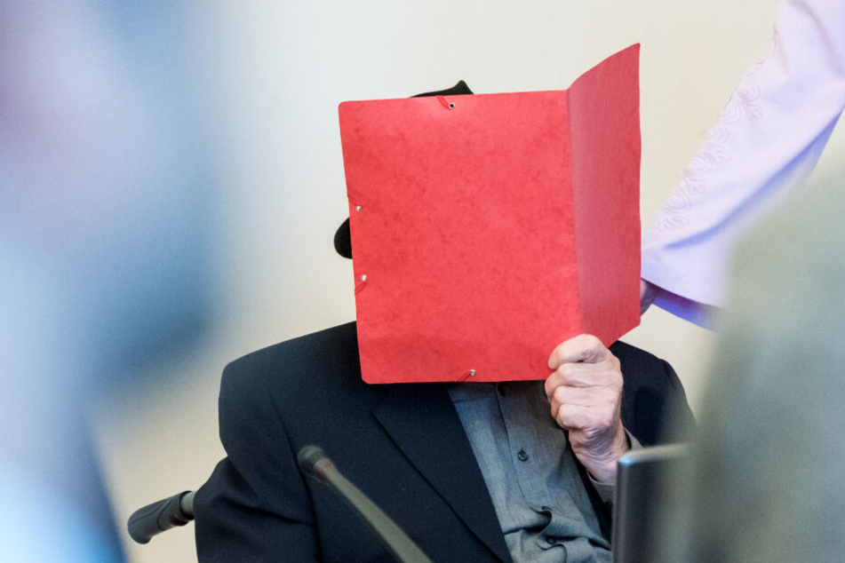 Der Angeklagte verbirgt sein Gesicht hinter einem Aktenordner.