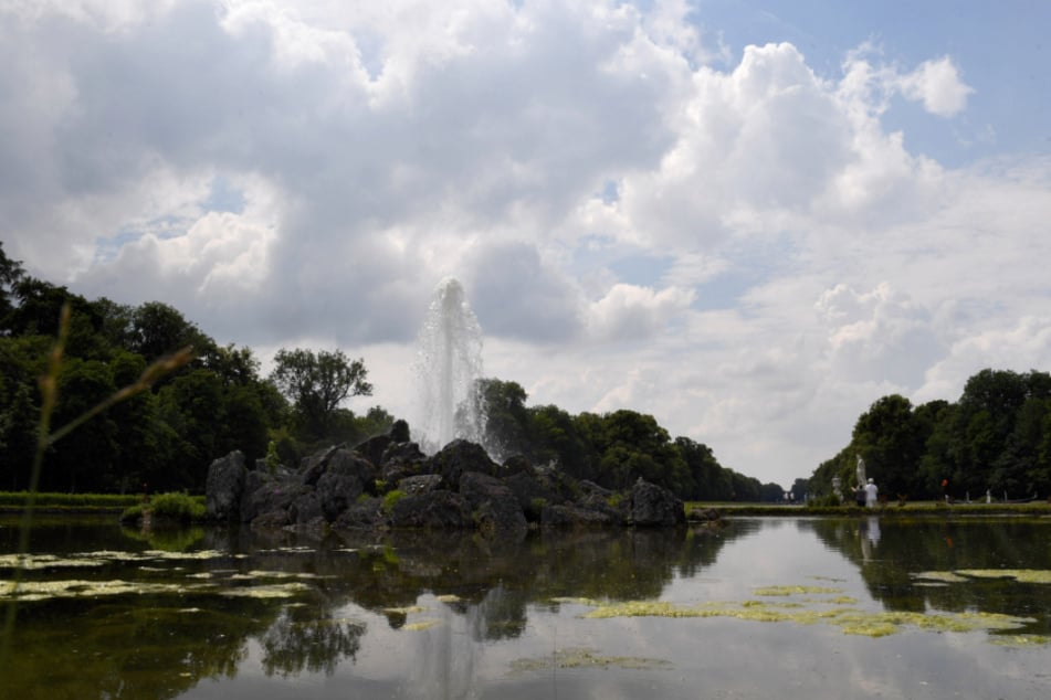 Die Fontäne eines Springbrunnens ist im Schlosspark Nymphenburg in München bei bewölktem Himmel und Sonne zu sehen.