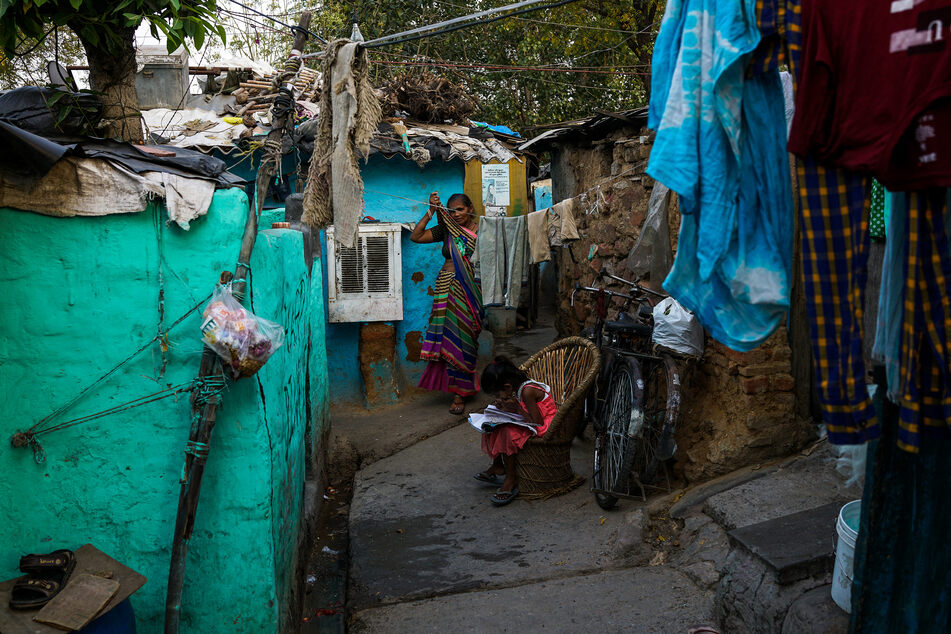 Eine Frau hängt in einem Slum in Neu-Delhi Wäsche auf, während ein Kind auf einem Stuhl sitzt und lernt. Im Zuge der "Verschönerung" der Stadt verloren Zehntausende Menschen vor dem G20-Treffen ihre Häuser. (Archivbild)